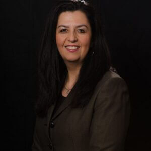 Portrait of a smiling woman in a dark suit, black background.