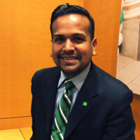 Business professional in suit and green tie, smiling, seated in office setting.